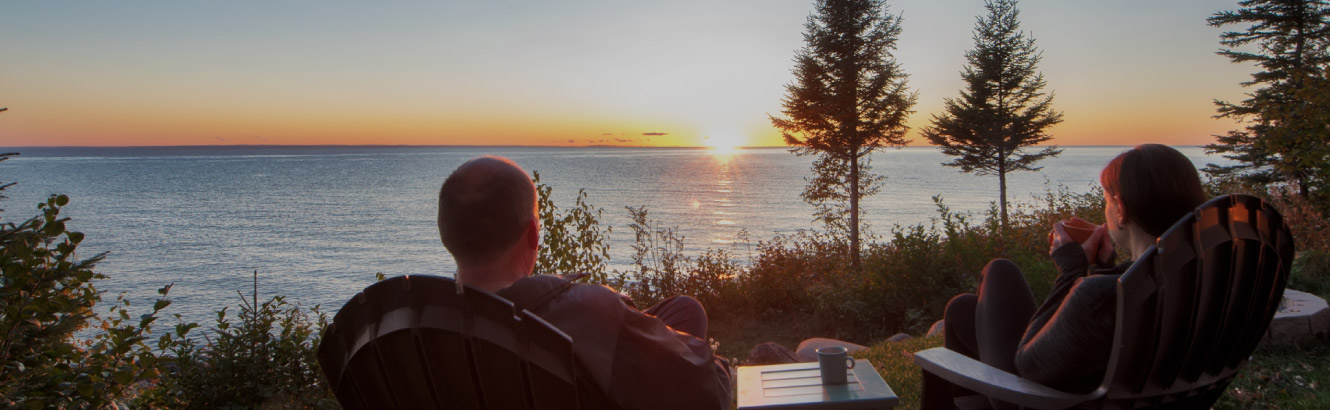 Man and woman sit in lawn chairs enjoying the morning sun appearing over the lake. 